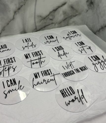 13 acrylic baby milestone plaques with handwritten phrases on a marble surface